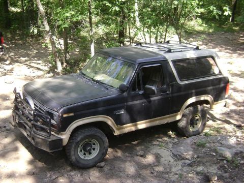 1990 Ford Bronco - This Ford Bronco is parked on a dirt trail surrounded by trees.