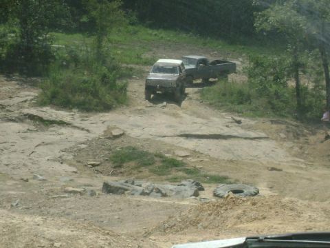 1990 Ford Bronco - Off-road vehicles tackle a challenging rocky incline on a sunny day.