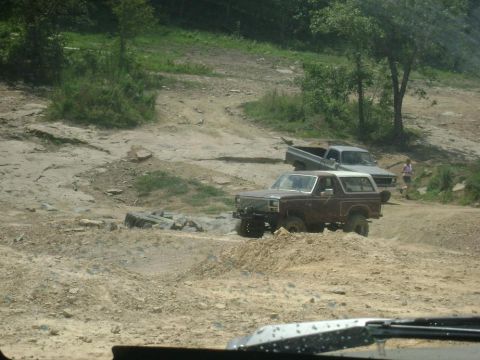 1990 Ford Bronco - A brown Ford Bronco navigates a rough off-road course with another truck in the background.