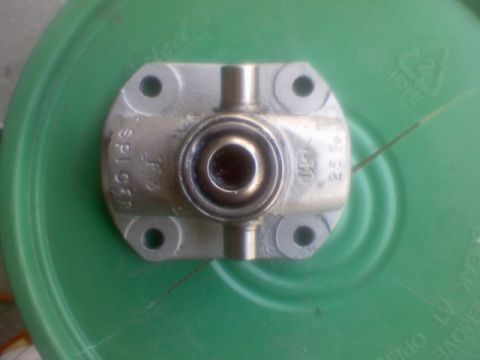 1996 Ford Bronco - Top-down close-up of a Spicer universal joint cross with a bearing cap installed, sitting on a green plastic bucket lid. The cast "SPICER"…