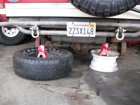 1991 Ford Bronco - Spare tire and wheel supported by jack stands under the rear axle of a vehicle.