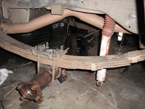 1991 Ford Bronco - Close-up view of the rear axle, leaf springs, and a red-booted shock absorber on a vehicle.