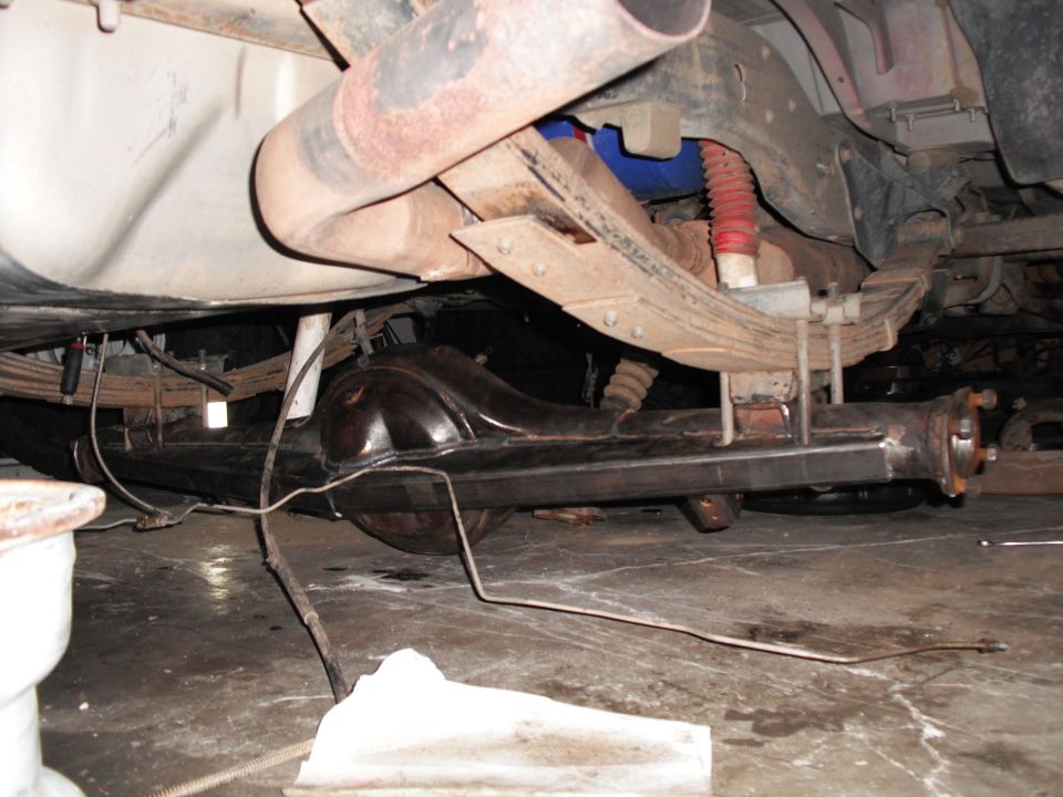 Underside view of a trussed leaf-sprung rear axle with red shock and muffler
