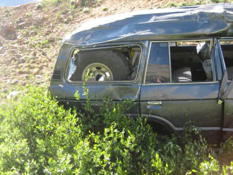 1978 Ford Bronco - A damaged dark SUV sits partially obscured by foliage on a rocky hillside.