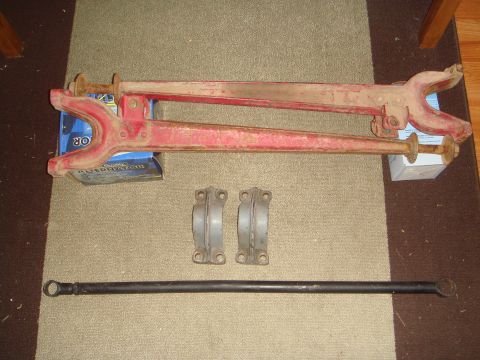 1992 Ford Bronco - Several automotive suspension components, including red control arms and a black tie rod, are displayed on a carpeted surface.