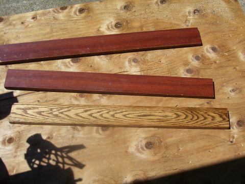 1991 Ford Bronco - Two dark red wood planks and one light brown wood plank with visible grain are arranged on a plywood surface.