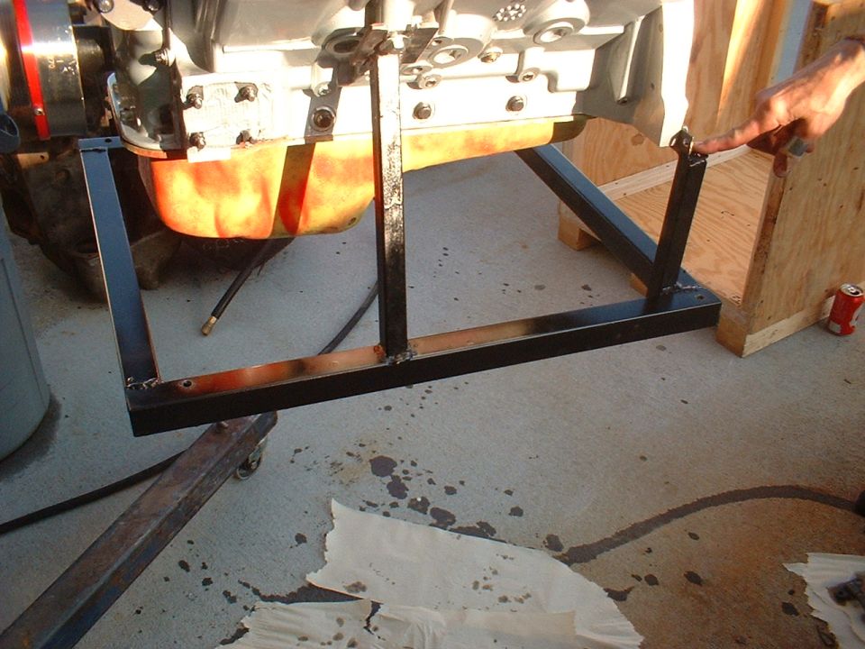 Engine on a metal stand, being worked on. A hand points to a bracket