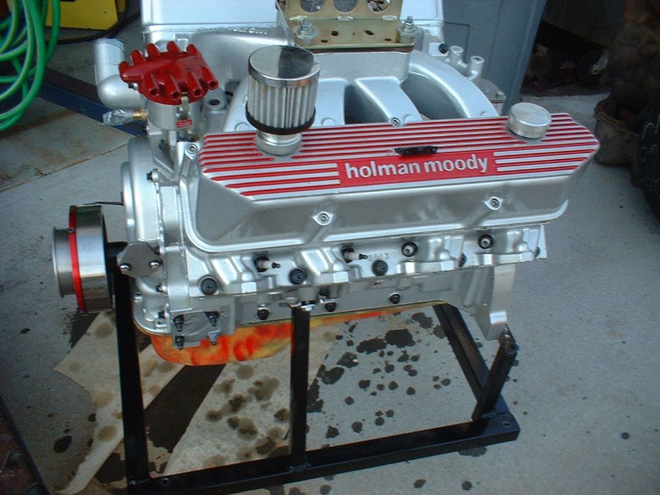 Engine with Holman Moody valve covers on a stand, showing oil stains on the ground