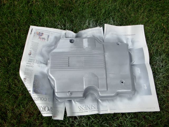 Silver freshly painted engine cover drying on newspaper over grass