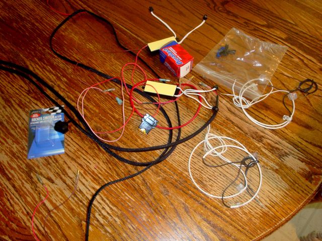 Automotive wiring, relays, and switch components laid out on wood floor