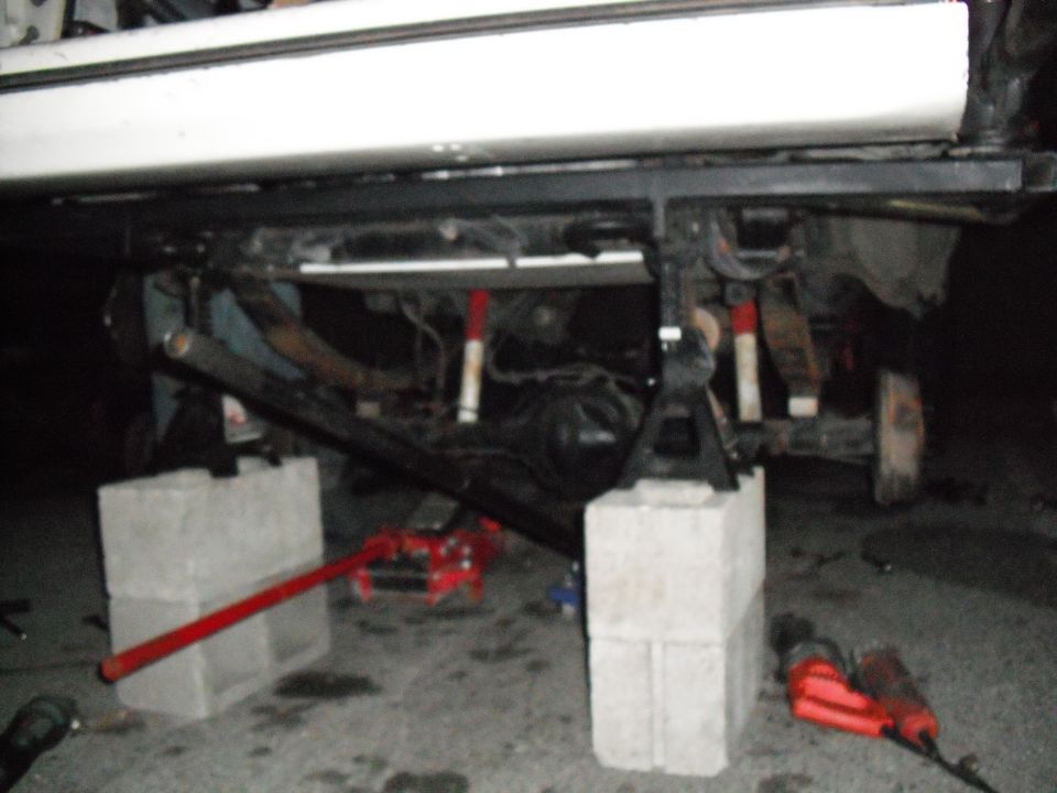 1991 Ford Bronco undercarriage supported by jack stands and cinder blocks, with a red floor jack visible