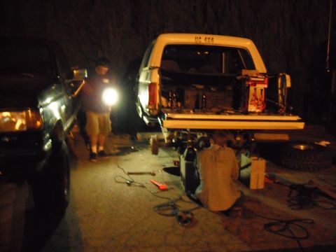 1991 Ford Bronco - People are working on a lifted truck at night, with tools and equipment scattered around.