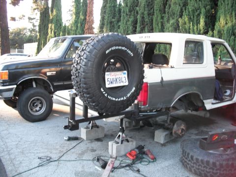 1991 Ford Bronco - Two Ford Broncos are parked outside, one is being worked on with its rear axle removed.