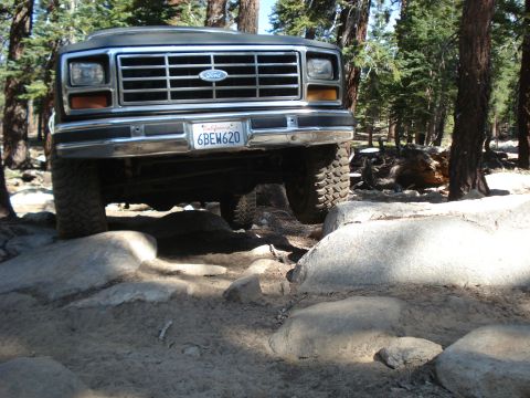 1984 Ford Bronco - A Ford Bronco navigates a rocky trail, its front grille and license plate clearly visible.