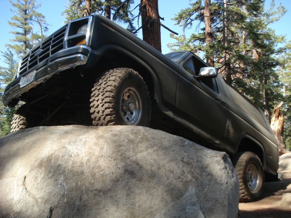 Dark SUV with off-road tires on a large rock, front grille visible