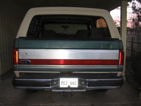 1989 Ford Bronco - The rear of a Ford Bronco is parked under a carport, showing its license plate and taillights.