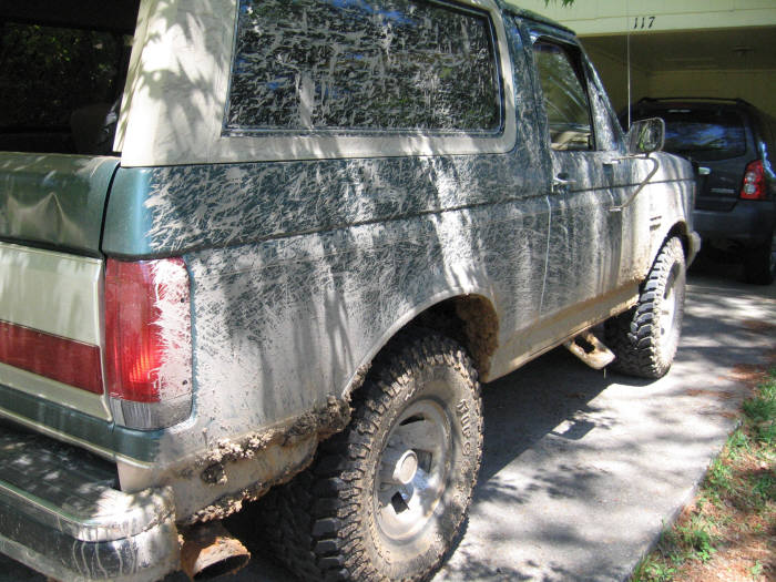 Mud-splattered green and tan Ford Bronco, rear quarter panel visible, with aftermarket wheels and tires