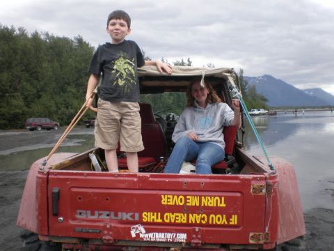 1987 Suzuki Samurai - A Suzuki Samurai with two children in the back is parked near a body of water with mountains in the background.