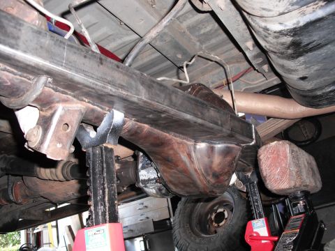 1991 Ford Bronco - Close-up view of a vehicle's undercarriage, focusing on the axle and fuel tank assembly, supported by red jack stands.