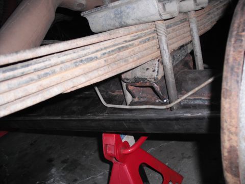 1991 Ford Bronco - The underside of a vehicle, focusing on the leaf spring and frame components, supported by a jack stand.