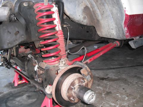 1991 Ford Bronco - Close-up of a vehicle's front suspension and brake system, showing aftermarket red springs and a Rancho shock.