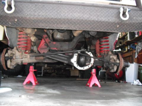 1991 Ford Bronco - The front axle and suspension components of a vehicle are visible while it is supported by jack stands.