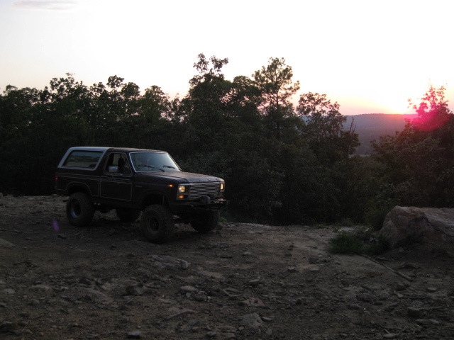 Dark 1980 Ford Bronco with off-road tires on a dirt hill at sunset