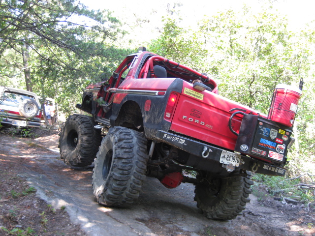 Red Ford Bronco with large tires on a dirt trail, another vehicle visible behind it