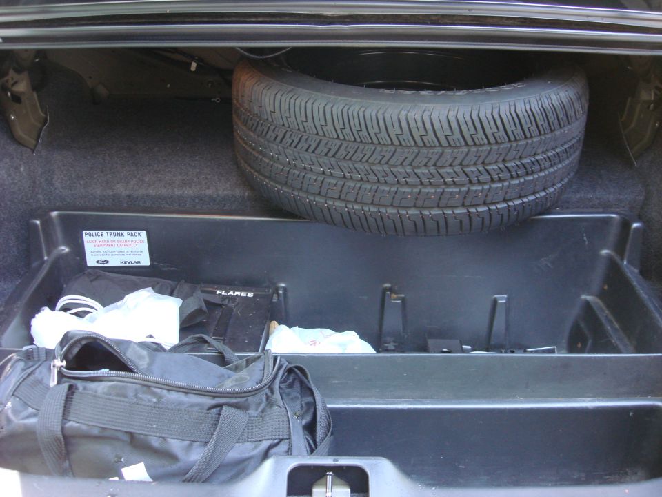Trunk of a car with a spare tire, duffel bag, and a police trunk pack containing flares and other equipment