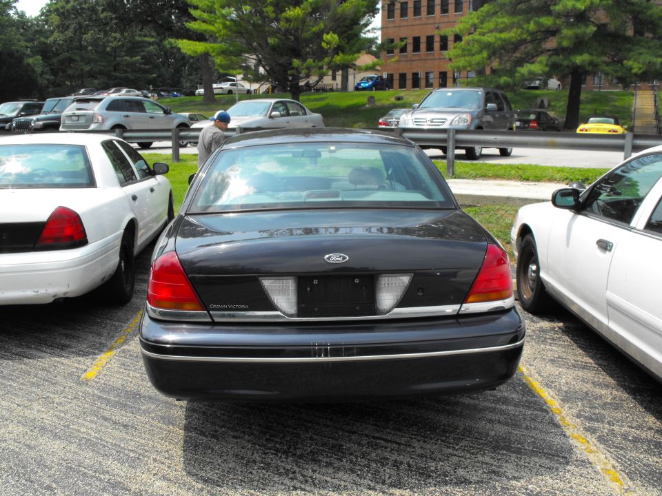 Rear view of black Ford Crown Victoria sedan parked between white sedans in a parking lot
