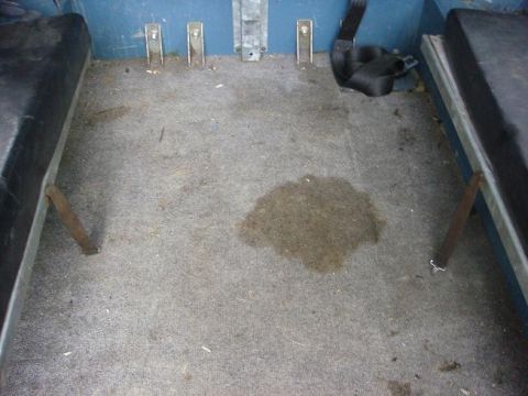 1972 Land Rover Land Rover - The interior of a vehicle shows worn grey carpet with a dark stain and two black seats.