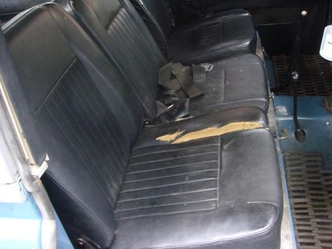 1972 Land Rover Land Rover - The interior of a 1972 Land Rover shows worn black vinyl seats with a torn section on the passenger seat.