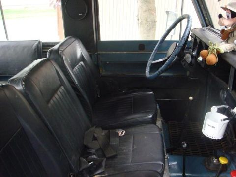 1972 Land Rover Land Rover - The interior of a blue vehicle features black vinyl seats and a blue steering wheel, with a view of the dashboard and floor controls.
