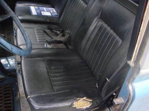 1972 Land Rover Land Rover - Interior of a blue vehicle showing worn black vinyl seats and a blue steering wheel. A manual is visible on the passenger seat.