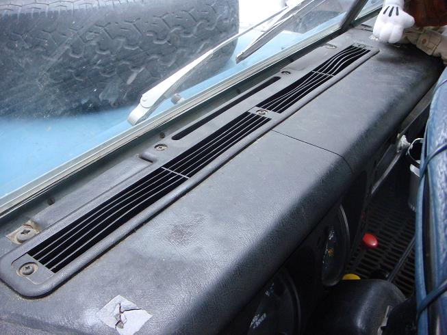 Dashboard vents and windshield wipers visible inside a vehicle. Spare tire is in the background