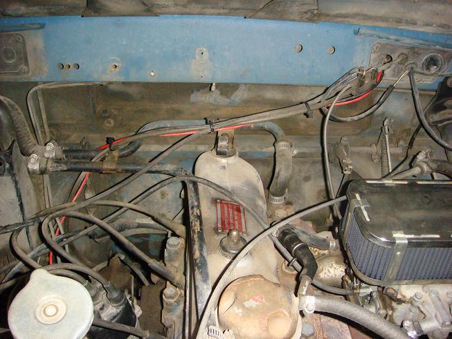 Engine bay with hoses, wires, and a filter. Red tag on engine block