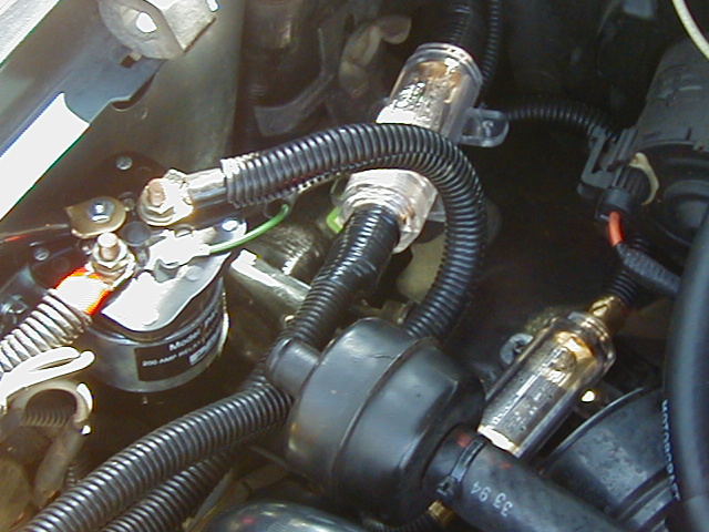Engine bay with 200-amp relay, black loomed wiring, and two clear inline fuse holders