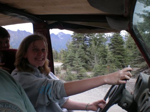 1987 Suzuki Samurai - A young woman smiles while driving a vehicle on a dirt road through a mountainous, forested area.