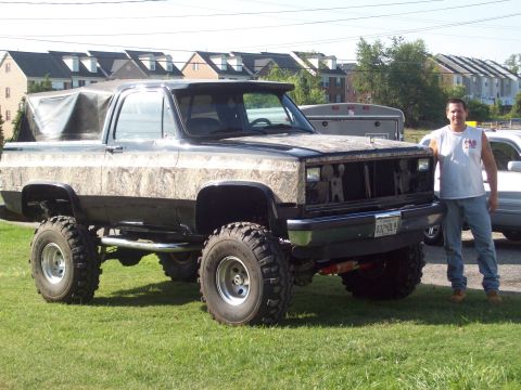 1948 Jeep Wrangler - This heavily modified SUV features a camouflage body wrap and a unique grille, standing on a grassy field.