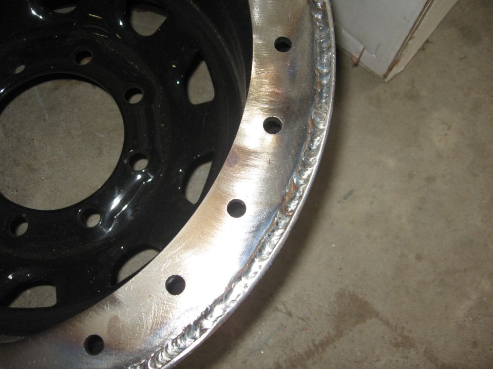 Close-up of a black steel wheel rim with a welded silver outer lip and multiple bolt holes
