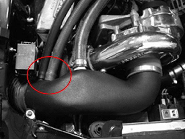 Close-up of engine bay components, including a turbocharger and intake piping, with a red circle highlighting a hose connection