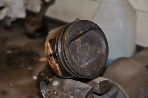 1996 Ford Bronco - A used piston, likely from an engine rebuild, is clamped in a vise for inspection.