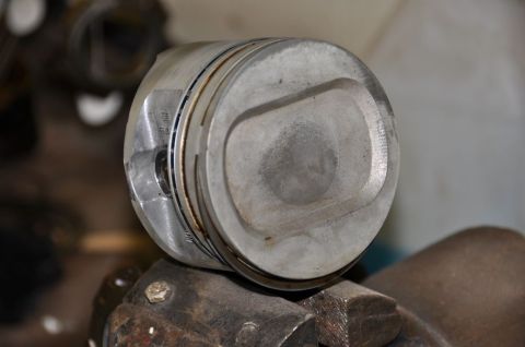 1996 Ford Bronco - A close-up view of a single engine piston, clamped in a vise, with visible piston rings and some wear marks.