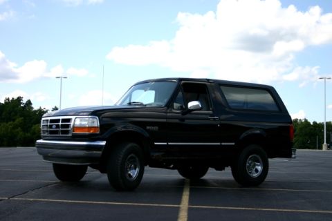 1995 Ford Bronco - This black Ford Bronco is parked in an asphalt lot with trees and light poles in the background.
