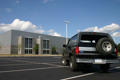 1995 Ford Bronco - A black 1995 Ford Bronco is parked in an empty lot with a modern building in the background.
