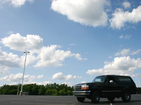 1995 Ford Bronco - A black 1995 Ford Bronco is parked in an empty lot under a bright, cloudy sky.