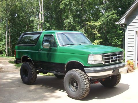 1992 Ford Bronco - A lifted green 1992 Ford Bronco with aftermarket wheels sits parked in front of a house.