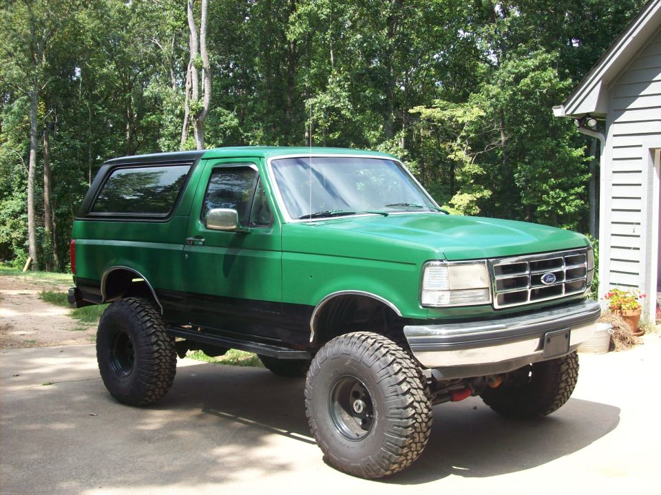 Lifted green Ford Bronco with black top, passenger front three-quarter view on driveway