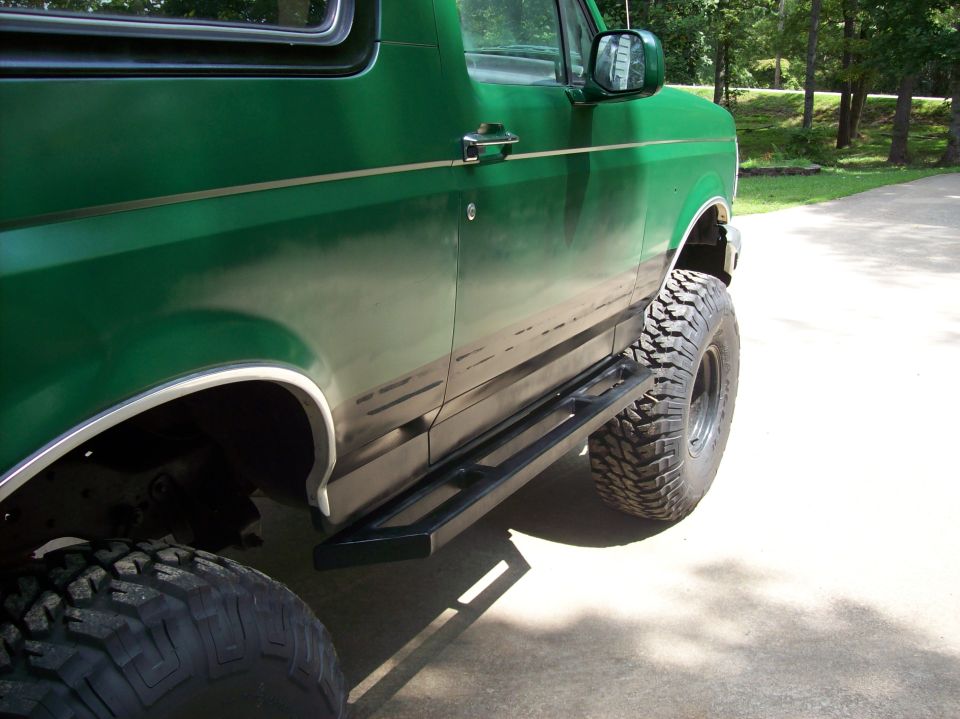Green lifted Ford Bronco passenger side with black tube step bar and mud tires