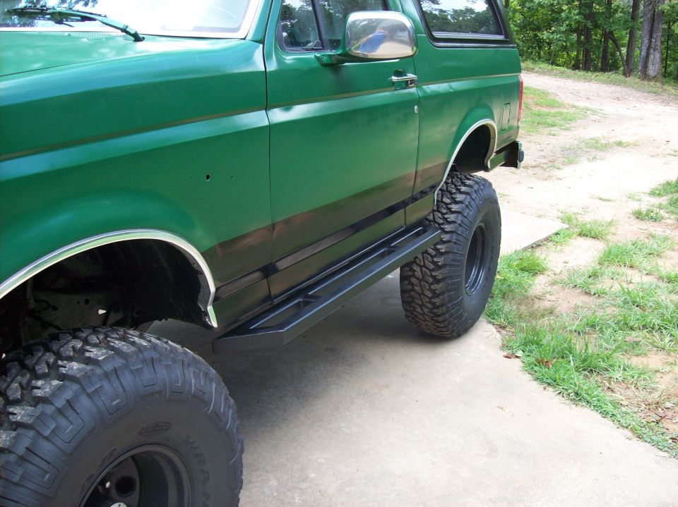 Green lifted Ford Bronco side view with black rock slider and mud-terrain tires